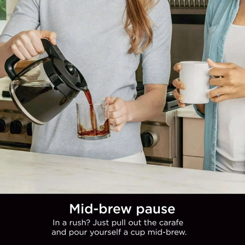 Person pouring coffee from a 12-cup programmable coffee maker with glass carafe into a cup, showcasing mid-brew feature.