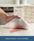 White microfiber cleaning cloth; close-up of hand wiping a kitchen counter.