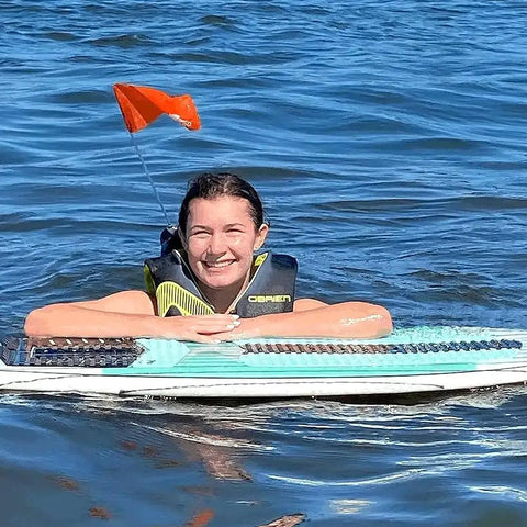 Person swimming with a bright orange life jacket safety flag with adjustable pouch and universal straps, visible above the water.