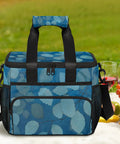 Blue Insulated Picnic Backpack Lunch Bag For Men And Women Grab And Go Portable Tote with leaf design on picnic table.