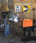 Welder using 3 Tier Rolling Welding Cart for Mig Tig Arc Plasma Cutter Machines in a workshop, holding tools and equipment.