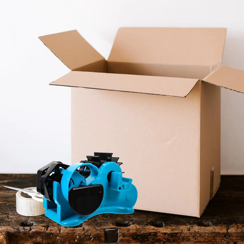 Semi Automatic Heat Tape Cutter With Compact Desktop Packing Station And Lightweight Tape Holder For Quick Box Sealing And Top Shelf Shipping Hustle The Reliable Gadget For Smooth Tape Dispensing Routine Blue on a wooden surface next to an open cardboard box.