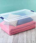 Badass 105 Quart Clear Plastic Storage Bin With Snug Blue Latching Lid Stackable Heavy Duty Box filled with bedding and pillows.