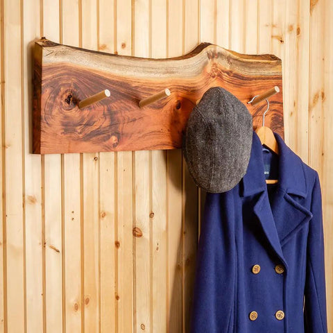Wooden coat rack with hooks, grey hat, and blue coat hanging on a light wood-paneled wall