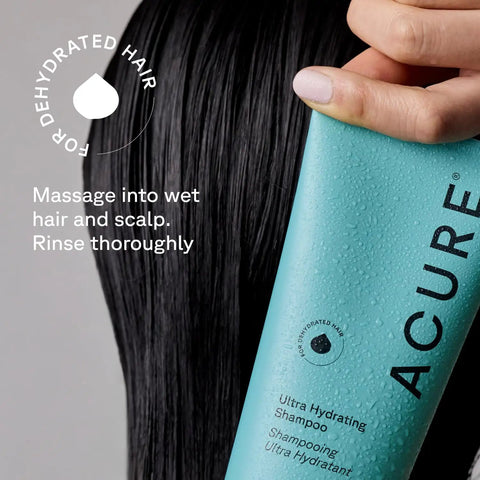 Close-up of a hand holding Acure Ultra Hydrating Shampoo for all hair types with droplets, perfect for locking in moisture.
