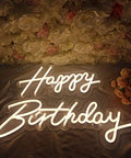Two Piece Happy Birthday LED Neon Sign Set 24 Inch And 18 Inch Warm White Glow displayed against floral backdrop