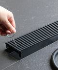 Hand removing grate from 32 Inch Linear Shower Drain With Removable Wedge Wire Grate Matte Black 304 Stainless Steel Rectangle Floor Drain For Bathroom Cupc Certified Hair Strainer No Clog Easy Clean High Flow 50 To 60 Liters Per Minute With V Shaped Slope.