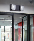 LED Emergency Lights With Battery Backup Four Pack Black Two Head Adjustable Emergency Exit Light Fixtures For Business UL Listed AC 120 277V Hardwired mounted above glass doors in a commercial hallway.