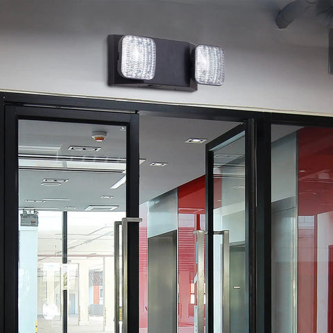 LED Emergency Lights With Battery Backup Four Pack Black Two Head Adjustable Emergency Exit Light Fixtures For Business UL Listed AC 120 277V Hardwired mounted above glass doors in a commercial hallway.