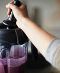 Person using Low Profile Tamper For 64-Ounce And 40-Ounce Containers BPA-Free Plastic Top Rack Safe And Dishwasher Safe Design Helps Fully Incorporate Thick Mixtures And Ingredients For Ultra Smooth Blends In A Breeze to blend smoothie in a blender