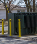 Heavy Duty Beefy Steel Safety Barrier Bollard And Industrial Traffic Control Post With Rock Solid Bright Yellow Finish And Concrete Fillable Base Plate For Warehouse Machine Guard At 42 Inches in urban setting next to electrical transformer.