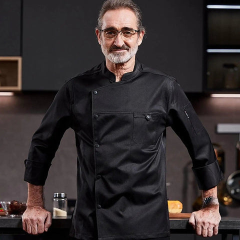 Heavy Duty Chef Coat With Chest And Sleeve Pocket Plus Hella Breathable Fabric That Keeps You Cool In The Heat worn by a middle-aged male chef in a modern kitchen.