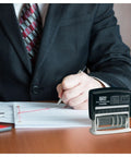 Slick Self Inking Micro Message Dater Stamp with Quick Flip Phrases for Office Organization on a desk with a suited professional.