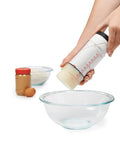 Two Cup Adjustable Measuring Cup With Grippy Rotating Body For Easy Pouring Of Peanut Butter And Honey in use over glass bowl