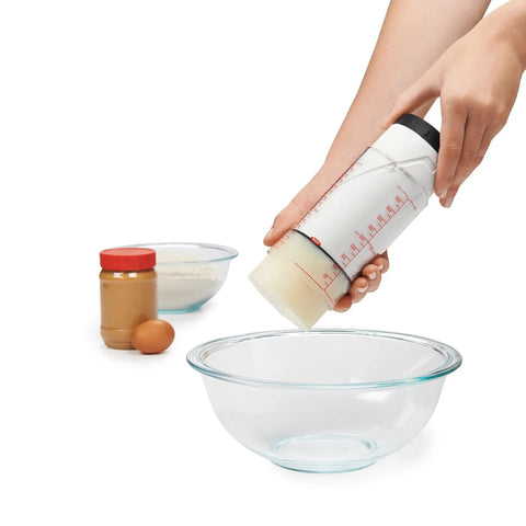 Two Cup Adjustable Measuring Cup With Grippy Rotating Body For Easy Pouring Of Peanut Butter And Honey in use over glass bowl