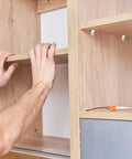 Hands adjusting shelf using Heavy Duty Glass Brackets Set With Suction Cups And Fixing Screws in a wooden cabinet.