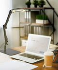 LED Magnifier Desk Lamp with Stand and Clamp next to a laptop on a desk, showing adjustable swivel arm, 5 diopter real glass lens