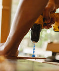 Close-up of a blue 25x125mm woodworking hole-opener drill bit installed in a yellow cordless drill drilling into wood