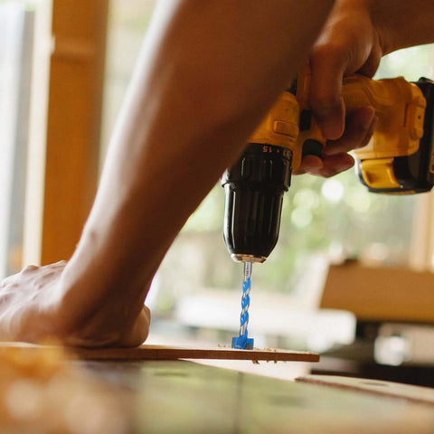 Close-up of a blue 25x125mm woodworking hole-opener drill bit installed in a yellow cordless drill drilling into wood