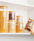 Airtight Glass Storage Jars Set Of 7 With Bamboo Lids For Pasta Cookies Nuts Coffee Beans Cereal Flour Pantry Organization BPA Free Clear Glass Canisters, neatly filled with pasta, beans, oats, and cereal on a shelf.