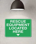 Green sign reading 'Rescue Equipment Located Here' under lamp; Equipment Storage Safety Caution Sign 8x12 Aluminum Plaque With Reflective Sheeting Rust Free Water Repellent Simple Mount For Factory Warehouse Emergency Gear Storage Area See It Clearly No Sweat.