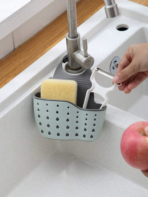 Double Deck Faucet Mount Kitchen Sink Organizer With Adjustable TPR Rubber Sponge Soap And Scrubber Storage Basket over sink, holding sponge and peeler.