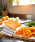 Orange crinkle vegetable cutter with stainless steel blade on cutting board, orange peels nearby