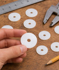 30 Piece Backyard Boss Nylon Flat Washers 1 1/4 Outer Diameter By 1 16 Inch Thick White Bulk Pack held in hand with measuring tools.