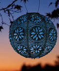Boho Outdoor Solar Lantern With Weatherproof Tyvek Fabric, dual white LEDs illuminating in a garden setting at sunset.