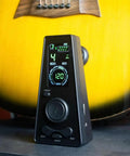 Digital Metronome For Piano Guitar Violin Ukulele Cello Flute With LED Display Rotary Tempo Knob in front of a guitar