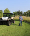 A person using a 40 Gallon Deluxe UTV Spot Sprayer With 2.2 GPM 70 PSI Max, mounted on a utility vehicle in a grassy field.