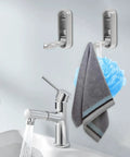 No Sweat Foldable Invisible Wall Hooks Zinc Alloy Storage Hangers 4 Pack mounted on bathroom wall holding towel and loofah.