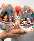 Miniature diorama inside a walnut shell showing a crafted scene with small figurines and furniture, hinged at the center.