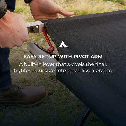 Person setting up heavy duty camping cot for adults with pivot arm for easy assembly outdoors.