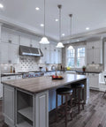 Modern kitchen with hanging lights, large island, bar stools, and stainless steel appliances under bright lighting.