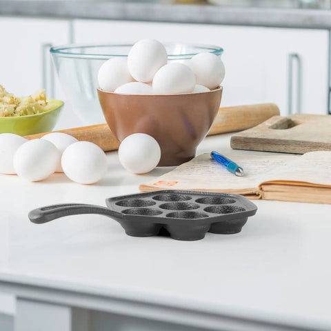 Seven Section Cast Iron Danish Aebleskiver Pan for Mini Puffs and Pancake Balls Preseasoned on kitchen counter with eggs and bowl