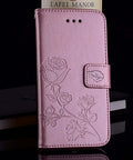 Pink floral embossed leather phone case standing upright on a table next to a glass, pen, and notebook.