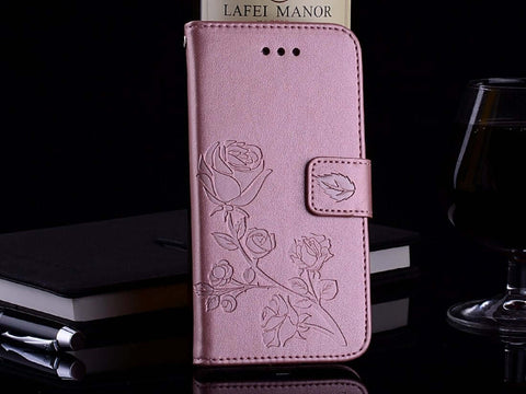 Pink floral embossed leather phone case standing upright on a table next to a glass, pen, and notebook.