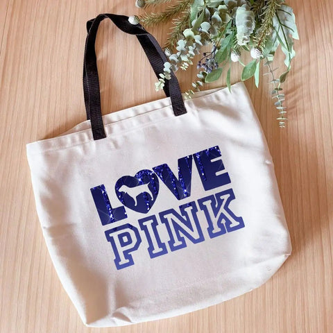 Canvas tote bag with blue 'LOVE PINK' text design, displayed on a wooden surface with greenery, showcasing Dope Color Sublimation Transfer Sheets For Heat Press Machine Pre Printed For Mugs Tumblers T Shirts And Tote Bags 12 Sheets 4.5 By 12 Inches No Edges Seamless Finish Ideal For DIY Custom Gifts.