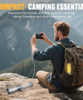 Man using smartphone with 2 In 1 Rechargeable Camping Lantern And Flashlight attached to backpack, mountains in background