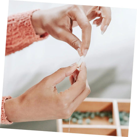Person threading a needle with clear string while using Level Up Your DIY Game With This Dope Bulk Lot Of Drilled Glass Spacer Beads.