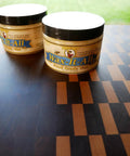 Real Deal Food Grade Beeswax Wood Polish And Cutting Board Wax, Zero Hustle Multi Surface Protectant That Keeps Kitchen Counters And Dining Tables Lookin Fresh, Smooth Finish Coating, Nine Oz Jar on a wooden cutting board.