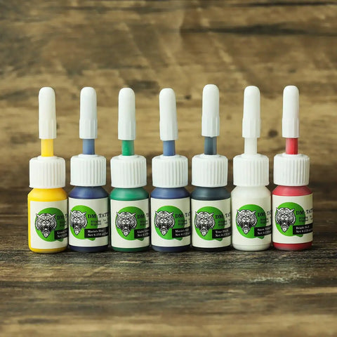 Color pack bottles for Four Coil Tattoo Machine Kit Set For Lining Shading And Coloring, assorted colors on wooden surface.