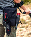 Person using metal detector with Heavy Duty Double Serrated Edge Digger With Sheath For Metal Detecting And Gardening A Tough As Nails Tool.