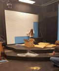 Person applying White 3D Brick Wallpaper Roll Set for Walls, Faux Brick Textured Stickers on a stage backdrop with blue panels.