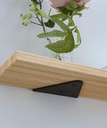 Rock Solid Heavy Duty Corner Brace Shelf Bracket Four Pack Built Tough As Nails To Hold Up To Seventy Pounds Forged From Quality Steel Comes With Screws For A Straight Up Hassle Free Home Improvement Upgrade. Black steel bracket supporting wood shelf with vase and greenery.