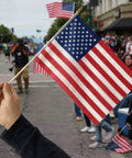 Person holding 12 Pack 8x12 Inch American Flags on Sticks for Outdoor Use with Grounded Multi Purpose Flagpole at parade.