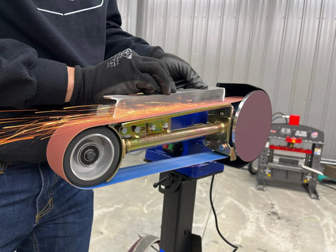 Hella Compatible 2X48 Belt Grinder Attachment Converts Standard Bench Grinder Into Rock Solid Vertical Or Horizontal Grinding Rig Featuring No Sweat Quick Change Tension System in use with sparks.