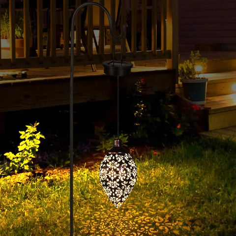 Olive Shaped Hanging Solar Lantern With LED Garden Lights illuminating a garden at night, weatherproof metal, outdoor decor.