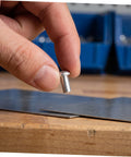 Person holding a solid aluminum dome head rivet above a metal sheet, showcasing the 200 Pcs Solid Aluminum Dome Head Rivets M5x10 for DIY projects.